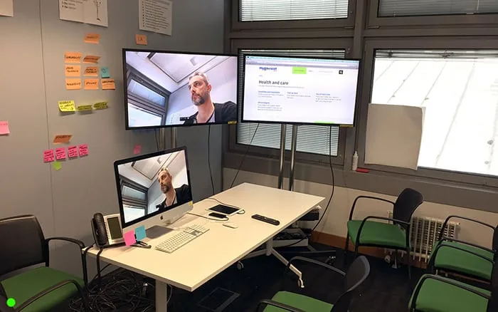 The observation room: two wall screens and an iMac showing the camera feed and the page being tested